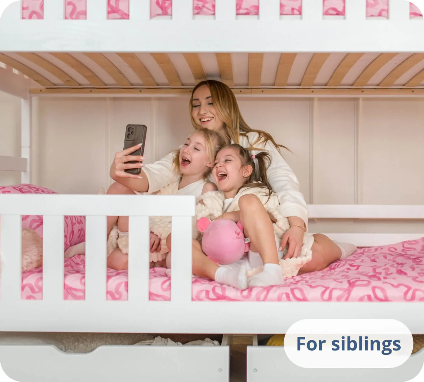 Two girls and a woman laughing at a phone on a white bunk bed.